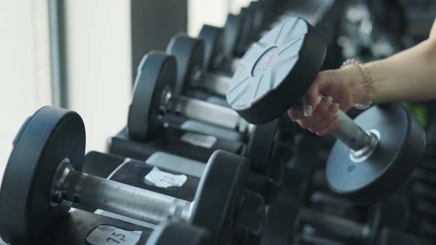 Close up shot of young sportive woman in sportswear taking dumbbell from stand in gym | Shutterstock HD Video #1029787949