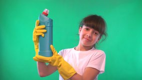 Girl in yellow gloves. In the hands of detergent. Direct gaze. Green background. Teenage girl. Dark hair.  The form of a man to the waist. White shirt. 4K video.