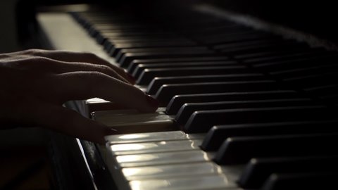 Woman pianist plays gentle classical music on a beautiful grand piano with one hand close-up in slow motion. Piano keys close up in dark colors. Student trains to play the piano