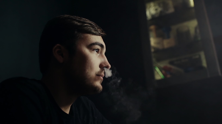 Close-up attractive guy smoking a hookah and blowing smoke rings at dark room of shisha lounge in slow motion. Young hipster man relaxing with his friends. Guys threw a bachelor party | Shutterstock HD Video #1029792635
