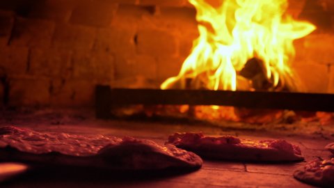 Restaurant chef Italian pizza is cooked takes pizza  in a wood fired oven at traditional restaurant.Close up pizza in firewood oven with flame behind being pulled from mobile wood fired oven  Video de stock