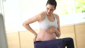 Pregnant woman at home sitting on fitness ball, trying to relieve pain