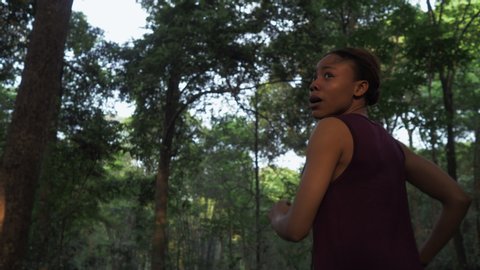 Fearful young African woman running in the forest camera fallowing Young girl been chasing in woods keep looking back Horrified Black woman lost in jungle 