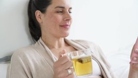 Pregnant woman laying on bed and drinking infusion