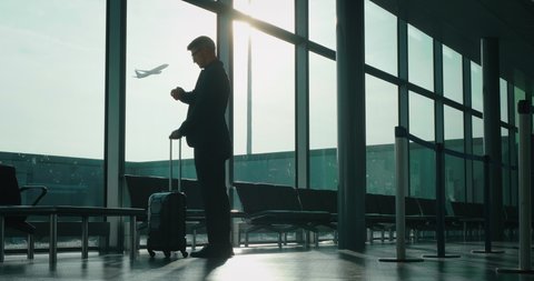 Slow motion of an young elegant businessman in a suit is walking with a suitcase in the international airport with a sunshine from the window.