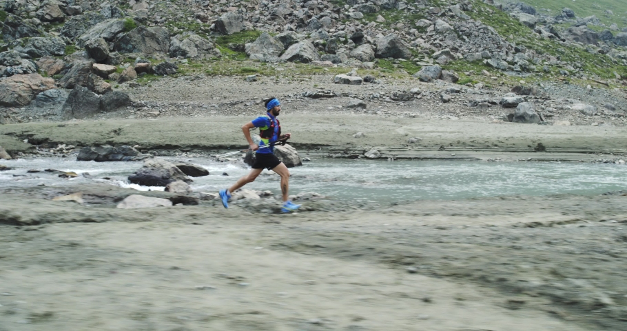 Man running near mountain creek river.Trail runner run to top peak training on rocky climb.Wild green nature outdoors in cloudy foggy bad weather. Activity,sport,effort,challenge,willpower concepts