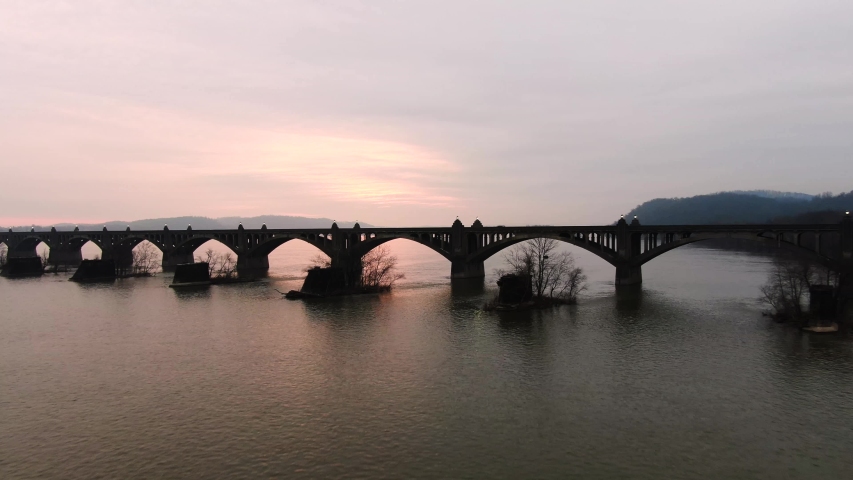 Aerial pull back from the North side of the Veterans Memorial Bridge where the pink and purple colors of the sunrise peak through the stone arches sit quietly in the Susquehanna River, southeastern PA