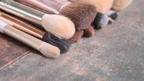 Close up footage of various used make up brushes on wooden board. Tracking shot. Selective focus.
