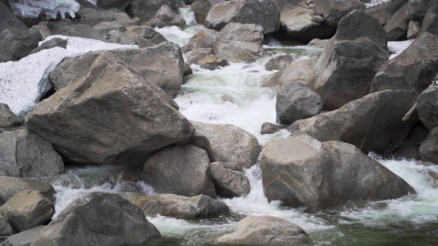 Slow motion rushing stream cascading over rocks and snow in Yosemite