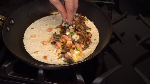 Cooking lacto-vegetarian quesadilla at home. Heating a tortilla in oil, adding layers of cheese and vegetables, folding the tortilla in half.