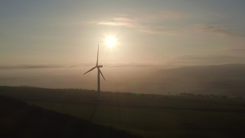 An aerial view of windfarm turbines slowly turning with the evening sun behind them, Aberdeensire, Scotland. Frame left to right.
