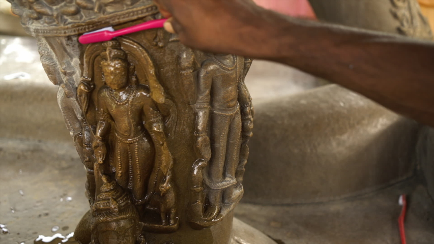 A hand held, close up shot of a person rubbing a statuette with a red toothbrush in an attempt to clean its crevasses.