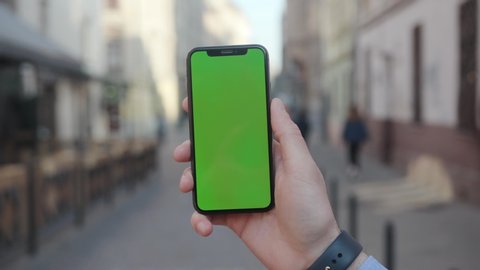 NEW YORK - April 5, 2018: On street man hands holding a smartphone with vertical green screen background city touchscreen wireless business evening cellphone communication device digital internet