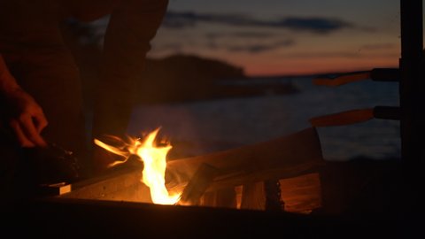 Man lighting camping fire by the sea at dusk