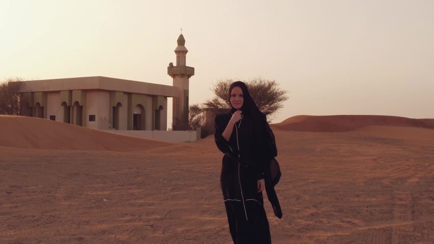 Muslim woman standing near mosque in the desert. Strong wind Middle East peace without war