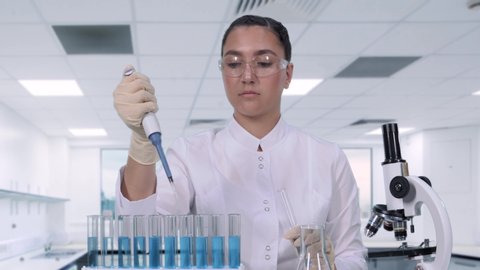A female scientist examines a blue liquid using a micropipette and test tube. A female researcher is conducting clinical trials. science lab