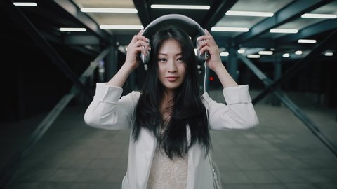 Asian woman puts on headphone walking at night underground