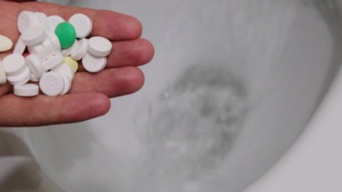 Slow motion men's hand with palm throws a lot of white pills into the toilet top view. close-up