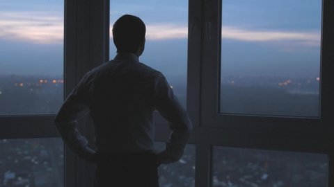 Back view of the thoughtful businessman wearing a suit looking out of the panoramic window. slow motion. 3840x2160