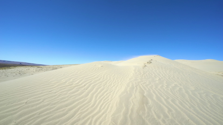 A man walks across a large sand dune in Wyoming. Wide shot.