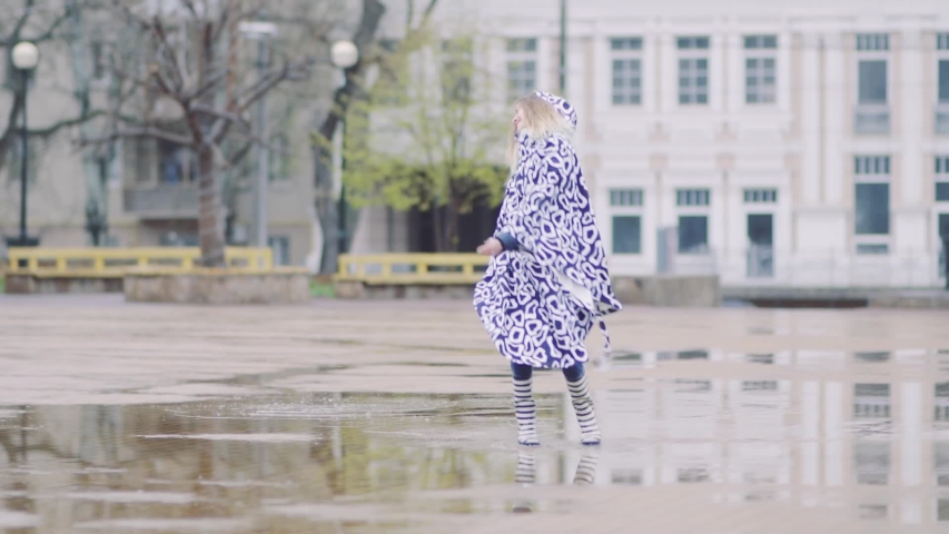 beautiful girl in rubber boots runs and jumps in a puddle after heavy rain. Woman having fun after the rain. Slow motion