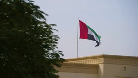 4K Dubai flag waving on top of a roof on a sunny day. The wind makes the fabric of the flag fly.