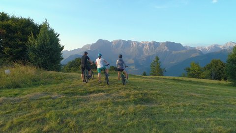 DRONE: Three mountain bikers stop and observe the picturesque morning landscape before exploring the Slovenian countryside. Young tourists riding ebikes stop to look around the scenic evening nature. - Βίντεο στοκ