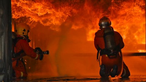 Firefighter on duty in Burning Building. Two firefighters fighting a fire with a hose and water during firefighting. Firefighters during battle and explosion of fire emergency case for danger mission