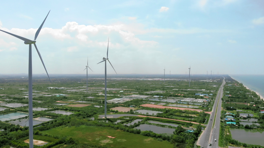 Wind turbine is generating electricity  power for people in a city near sea.Concept of clean power city for no pollution world.Clearly sky with cloudy with road and farming pool in city.Aerial shot. | Shutterstock HD Video #1029932564