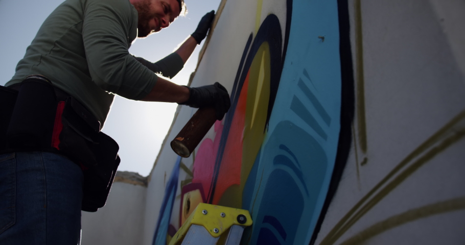 Low angle view of Caucasian graffiti artist painting with aerosol spray on the wall. He is using ladder
