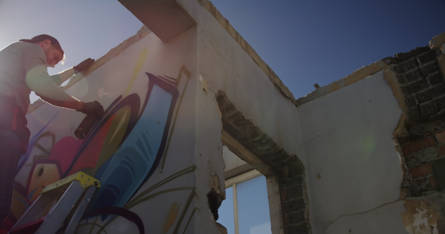 Low angle view of Caucasian graffiti artist painting with aerosol spray on the wall. He is using ladder