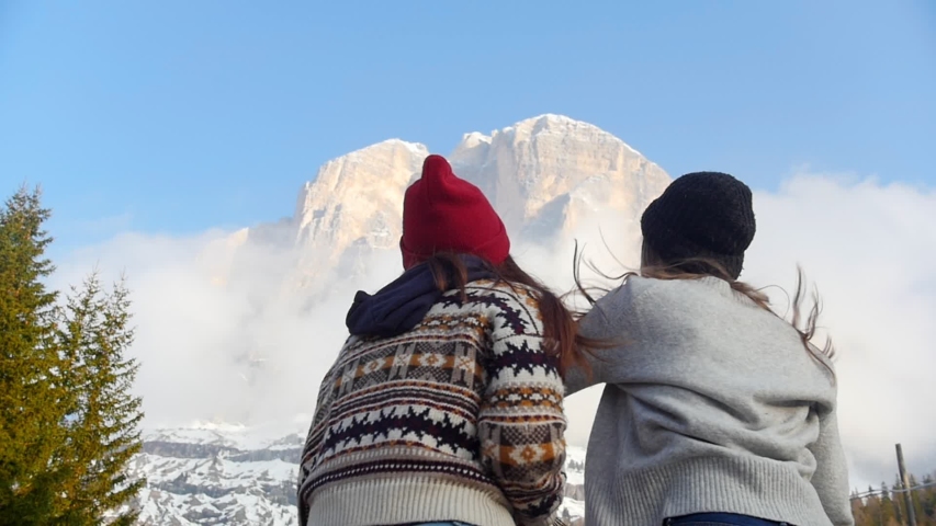 Two traveling happy young women jumping in front of the mountain