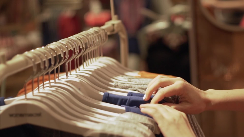Close up of a girl goes through clothes dresses summer outfits and shop the boutique, the supermarket on the rack, close-up of hands and racks of clothes, shopping