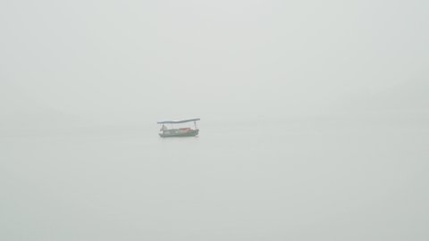 a single boat drifts on a lake in heavy fog