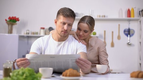 Young husband reading newspaper with wife drinking coffee, morning together