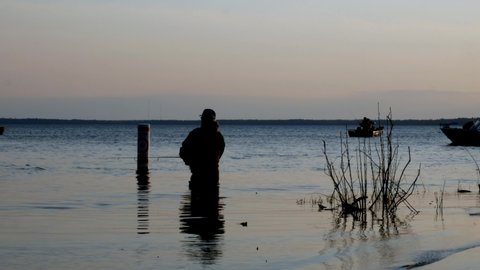 BEMIDJI, MN - 11 MAY 2019: Minnesota Fishing Opener. Wading fishermen standing in Lake Bemidji at the Mississippi River casts for walleye with men in boats on lake in background just after sunrise.