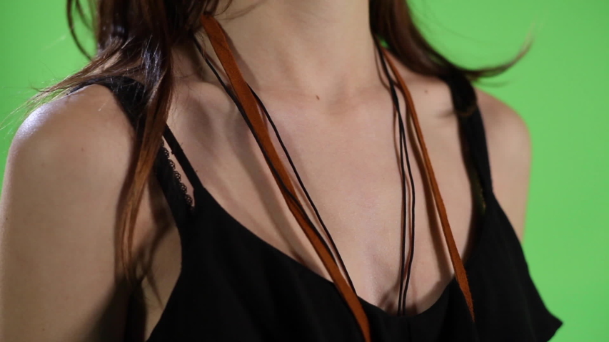 Close-Up shot of a female removing a necklace from around her neck with a key on it. Shot in front of a green screen.