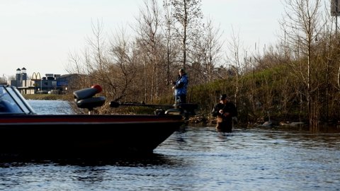 BEMIDJI, MN - 11 MAY 2019: Minnesota Fishing Opener. Motor boat glides by a wading fishermen standing in Lake Bemidji near bridge over the Mississippi River while he is reeling in a walleye.