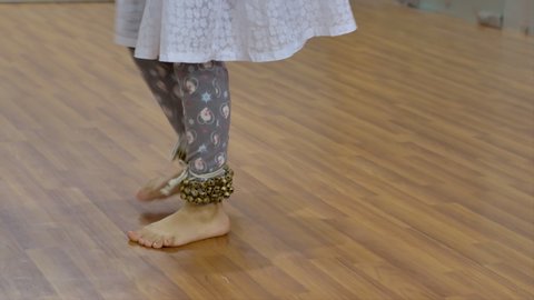 A little Indian girl wearing ghungroo practicing Kathak dance moves in the studio.