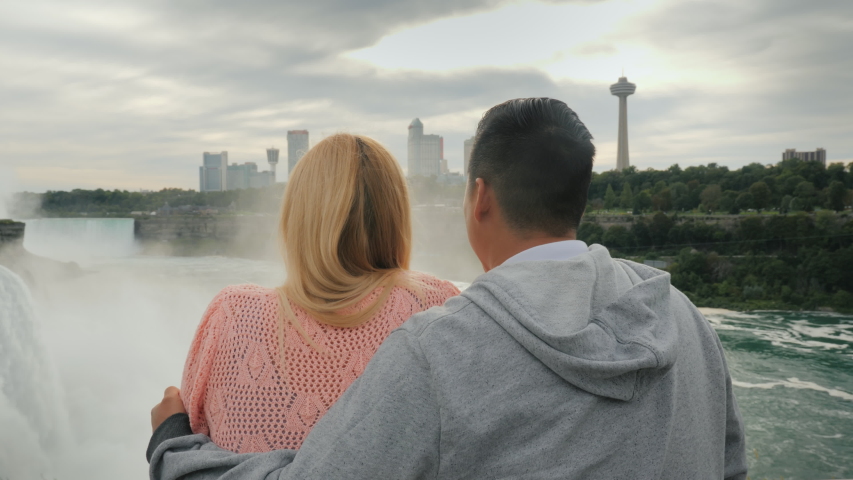 A young multi-ethnic couple looks at the famous Niagara Falls, enjoying the popular tourist attraction