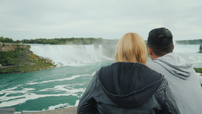 Active married couple spends a weekend at Niagara Falls, looking into the distance at the cascade of waterfalls