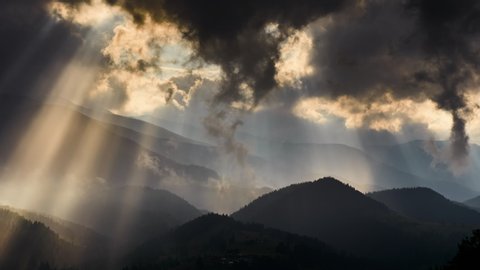 Timelapse of sun rays emerging though the dark storm clouds in the mountains 