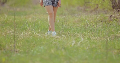 Girl in shorts and sneakers walks on the green lawn. Bottom view.