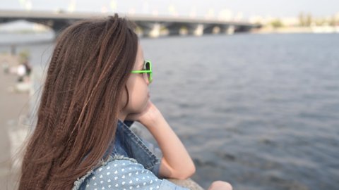 Girl in sunglasses near river
Portrait of adorable little brunette girl in sunglasses and denim suit sitting on column near river on sunny day