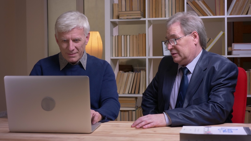 Portrait of old businessmen sitting together at the table working with laptop and discussing actively the project. | Shutterstock HD Video #1029977468