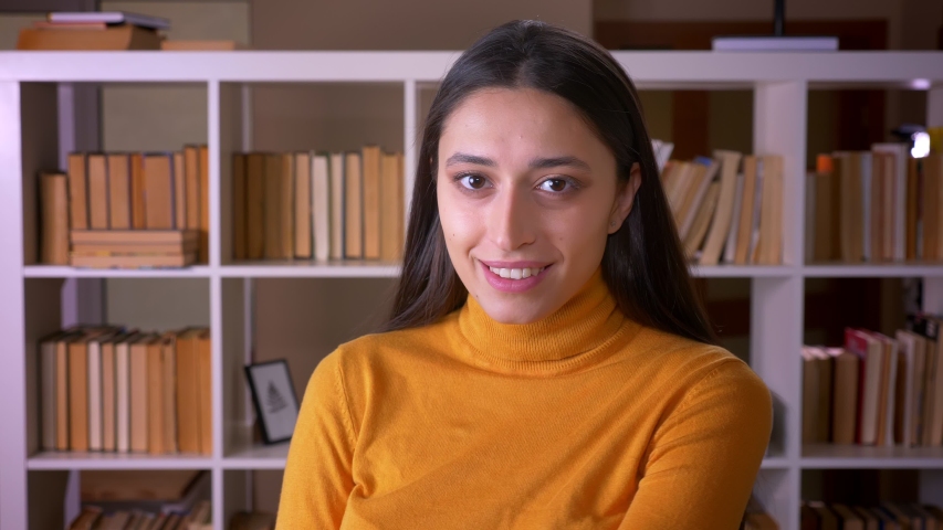 Portrait of pretty brunette female teacher smiles joyfully into camera and flirting with it at the library.