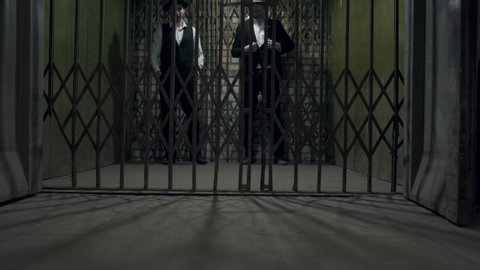 Two gangsters men in formal suits and fedora hat opening a metal forged gates