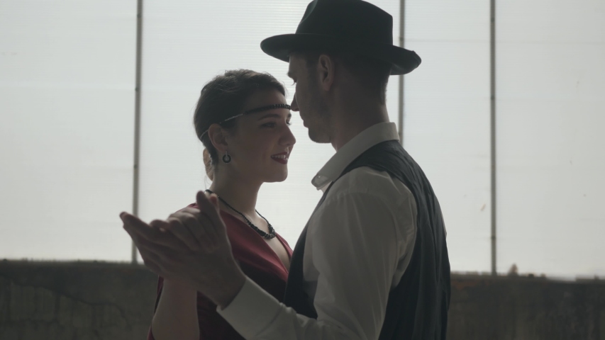 Man in fedora hat, classical suits and woman in style cloth dancing in dirty place. Abandoned dilapidated building. Self-confident businessman relaxing.