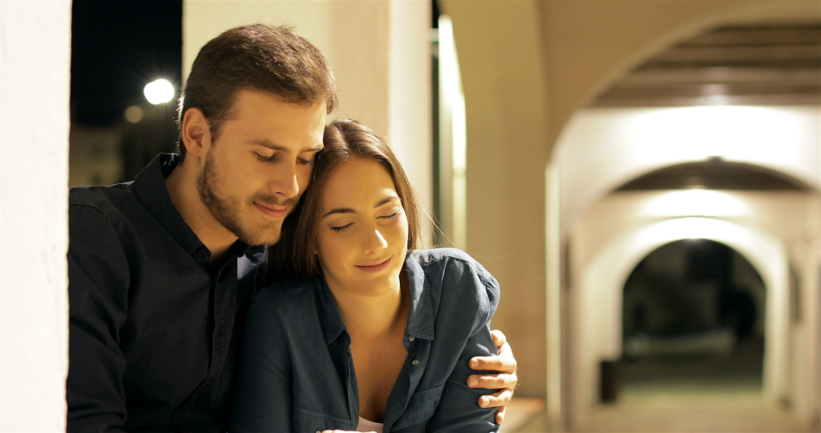 Happy couple in love hugging sitting in a town street the night