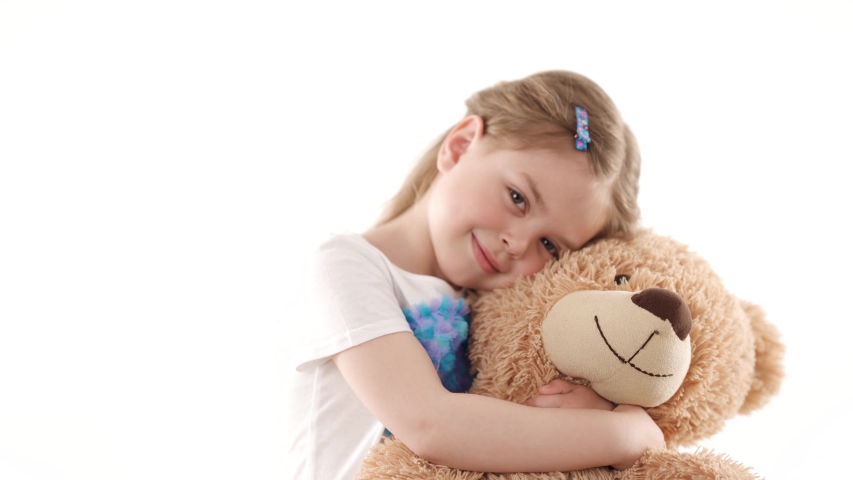 Video portrait of beautiful little girl smiles hugging a big bear toy. Video portrait of little girl isolated on white background. Happy childhood concept. Studio shot of child emotions in 4K.